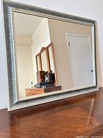 Front view of rectangular mirror with silver ornate frame on wooden surface