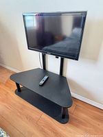 Front view of Samsung TV mounted on black corner stand with remote on shelf