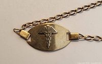 Close-up of oval ID plate with caduceus emblem and chain links