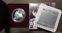 Coin in capsule within open presentation case beside certificate and sleeve