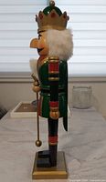 Left side view of wooden nutcracker king showing green coat, gold crown, faux fur, staff and base