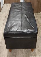 Closed ottoman front view showing faux leather surface and legs