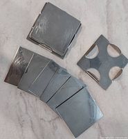 Stack of silver-tone square coasters with one holder showing circular cut-outs
