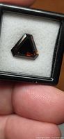 Triangular cut cognac orange tourmaline in black display box, frontal view