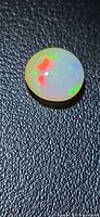 Round Ethiopian opal cabochon showing red and green play-of-color on black textured background