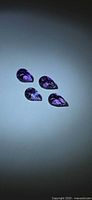 Four pear-cut purple amethysts arranged on a light blue background