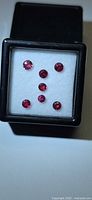 Front view of six round red gemstones in white foam within black display box