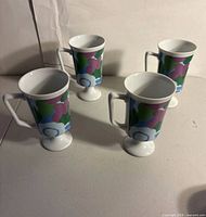 Front angled view of all four pedestal mugs showing floral pattern and pedestal bases