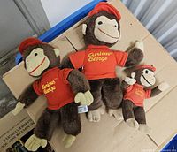 Group shot of three Curious George plush figures in different sizes
