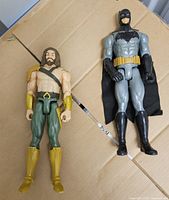 Batman and Aquaman figures side by side on cardboard