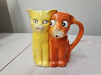 Front view of dual cat ceramic pitcher showing yellow and orange cat faces and handle