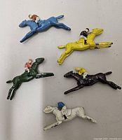 Five of the six painted cast metal horse and jockey figures in assorted colours
