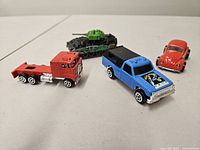 Group showing four vehicles: blue pickup, red Beetle, red truck cab, black/green tank