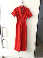 Full front view of red jumpsuit hanging, showing belt and zipper