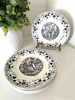 Stack of six black transferware plates with one displayed upright showing central scene and border