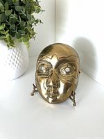 Front view of brass mask on stand
