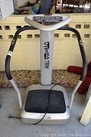 Front view of Vibra Trim exercise machine showing foot platform, handles and central support column with logo.