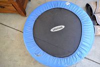 Top view of Exercera trampoline showing black jumping mat with logo and blue outer padding with wear marks.
