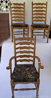 Three wooden dining chairs with ladder-back design, two side chairs and one arm chair with floral cushioned seats in natural wood finish.