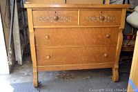 Front view of the wooden chest of drawers showing four drawers, two with floral decoration.