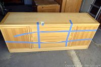Front view of maple-finish credenza with blue tape securing drawers and doors