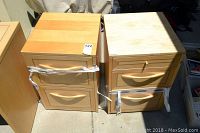 Two wood tone filing cabinets side by side, showing front and top surfaces with labels and some surface scuffs.