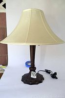 Full view of the table lamp showing beige fabric shade and decorative base with electrical cord.