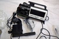 Photo of Canon VC-20 video camera with attached power cable, earphones, and carrying case on side.