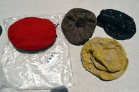 Four vintage berets arranged on a surface, showing red, brown, yellow, and dark blue colors with different textures and watch the 1940s Boy Scout beret as red.
