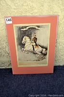 Framed painting showing a rider on a horse with a pink matte board, angled view