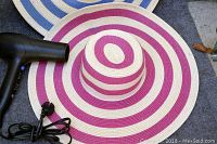 Photo showing a wide-brim hat with concentric purple and beige rings next to a black hairdryer.
