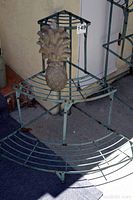 Front view of the green metal corner plant stand with the decorative pineapple on the middle shelf.