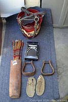Overhead view showing horse halter, leather quiver with vintage arrows, English stirrups in box, two vintage western stirrups, and vintage boys moccasins.
