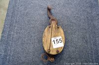 Vintage wooden pulley with metal hook, showing top view of oval wooden sides and rusted metal hardware on a gray surface.