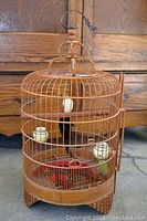 Front view of round bamboo birdcage with ceramic feeders and hand carved perch inside, showing cage structure and feeders.
