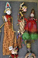 Photo showing all six traditional Indian puppets laid out on gray surface, displaying vivid costumes and detailed wood carved heads.