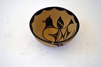 Top view showing interior black painted bird and leaf motifs on tan pottery bowl.