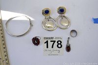 Photo showing sterling silver jewelry items arranged on white background with measuring ruler and lot number card. Items include silver bangle, lapis earrings, coral ring, amber pendant, black enamel ring, and small silver ring.