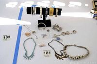 Overall photo showing a black bracelet display with six diverse bangles, multiple necklaces including a blue decorative necklace and silver chains, several bracelets including a chunky linked one, a gold-tone zebra brooch, and a small bag labeled cubic zirconia with earrings.