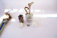 Overview of all items on white surface including milk white vase, smaller bird feeder, small candle holders, and dark decorative vase, with auction tags.