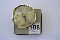 Front view of vintage brass barometer with clear dial, reading pressure units and weather indications