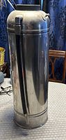 Cylindrical metal fire extinguisher showing side view with hose attached and missing top cap