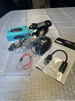 Group shot of all items: boxed Logitech mouse, two loose mice, DP-HDMI adapter in package, tripod mount, orange strap in case