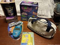 Overview of all five unopened items: Cuponk box, Shooting Stars gun box, travel ping pong bag, Radica Blackjack blister pack, Hilroy flash cards pack
