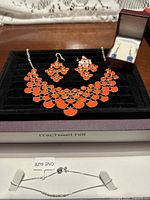 All four jewellery pieces displayed: orange necklace and earrings, blue drop earrings in box, silver bracelet in Michael Hill box