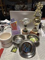 Group shot of all lot items including trophies, planter, vase, phone case, pet bowls, pyramid paperweight