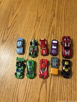 12 assorted die-cast toy cars laid out in two vertical rows on wooden surface