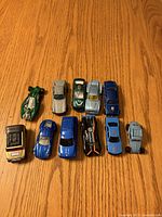 Top view of all eleven diecast toy cars arranged in two rows on wood surface