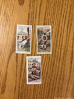 Fronts of three colour lithograph tobacco cards on wood surface