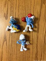 Front view of three Smurf figurines displaying distinct accessories